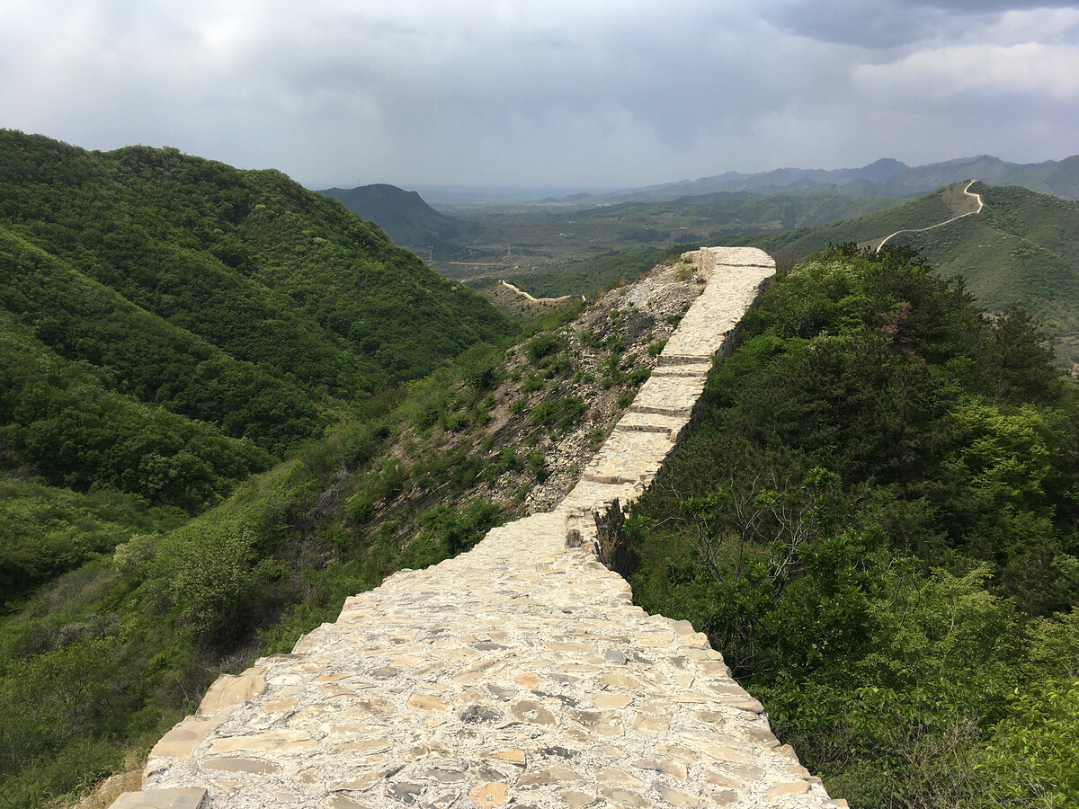 Great Wall in green hills, with stormy skies.