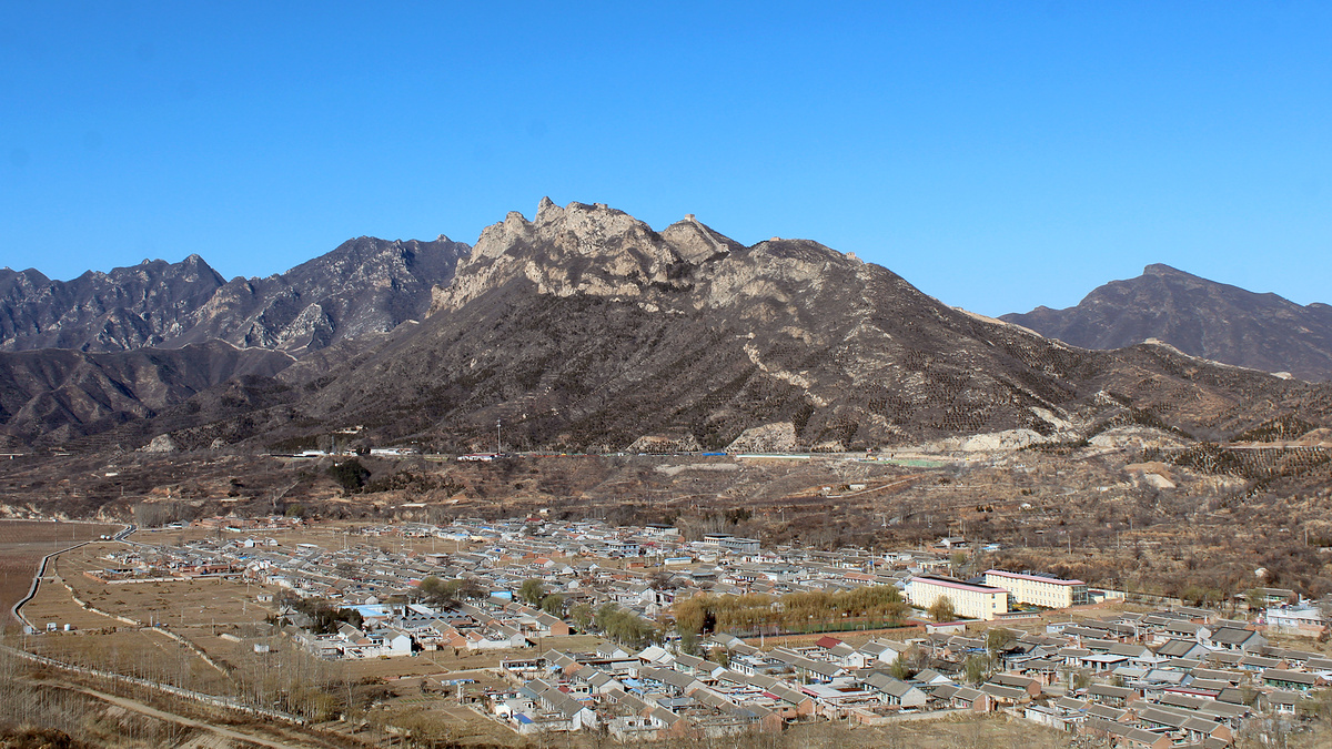 Great Wall towers atop tall cliffs, with a village below.